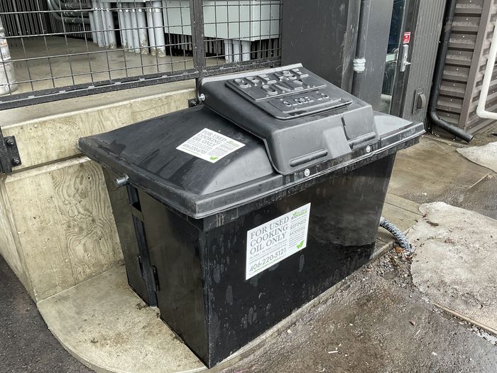 A black commercial dumpster beside a cleaned pad