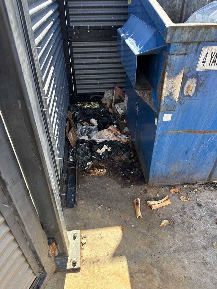 A commercial dumpster and enclosure before cleaning